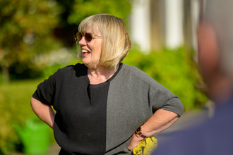 A lady is looking away from the camera laughing whilst stood outside amongst a green background.