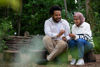 Trainees Nazia & von sitting on tree stumps surrounded by trees.