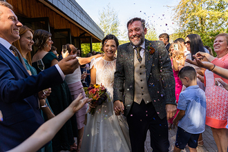 A bridge and groom walk through a group of people who are throwing confetti at them