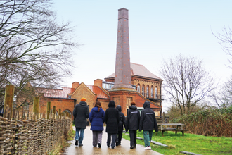 Group of young people walking in Walthamstow Wetlands towards the Engine House, with one of the Nature in Mind leaders.