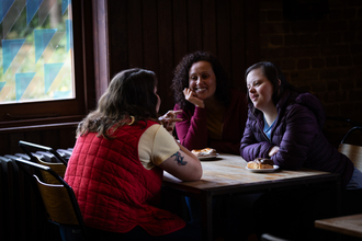 Three visitors sitting at a table eating pastries and drinking coffee at the Engine House Café, Walthamstow Wetlands.