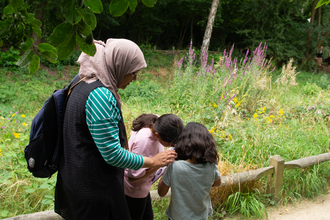 A mum with her two children standing by some greenery looking at pictures on a clipboard