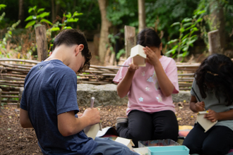 Three children sitting in the woodland area of Camley Street Natural Park decorating wooden bee hotels 