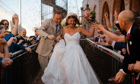 A couple who have just been married walk down an aisle and have confetti thrown at them 