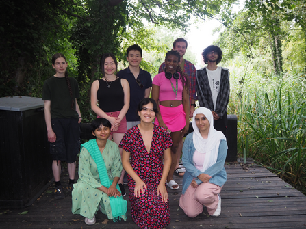 Nine youth board members smiling in a group photo on wooden decking by the pond at Camley Street Natural Park.