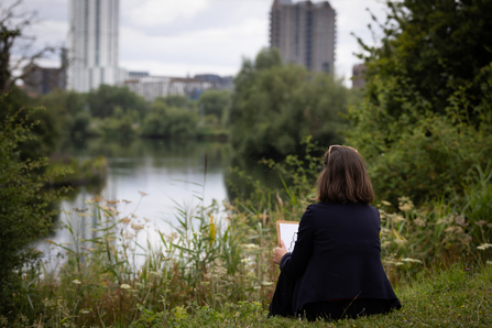 a person sat down holding a clipboard looking out at the wetlands