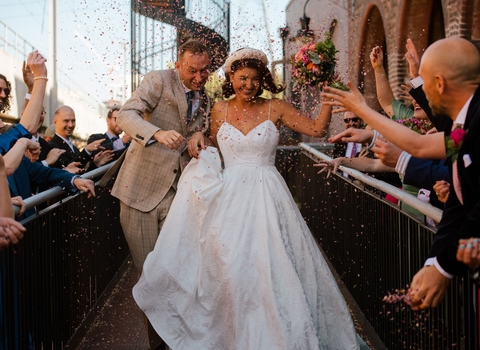 A couple who have just been married walk down an aisle and have confetti thrown at them 