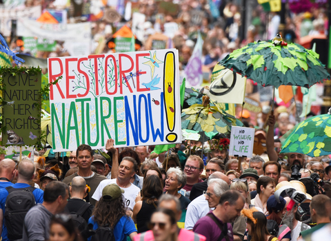 A large crowd of people with a large sign that says restore nature now