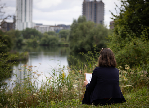 a person sat down holding a clipboard looking out at the wetlands