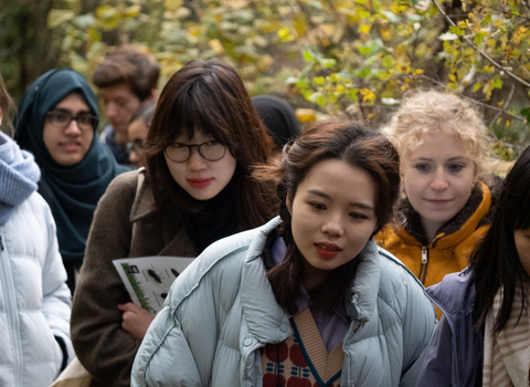 A group of young people gathered together holding wildlife identification material listening to a London Wildlife Trust staff member talk at Camley Street Natural Park.